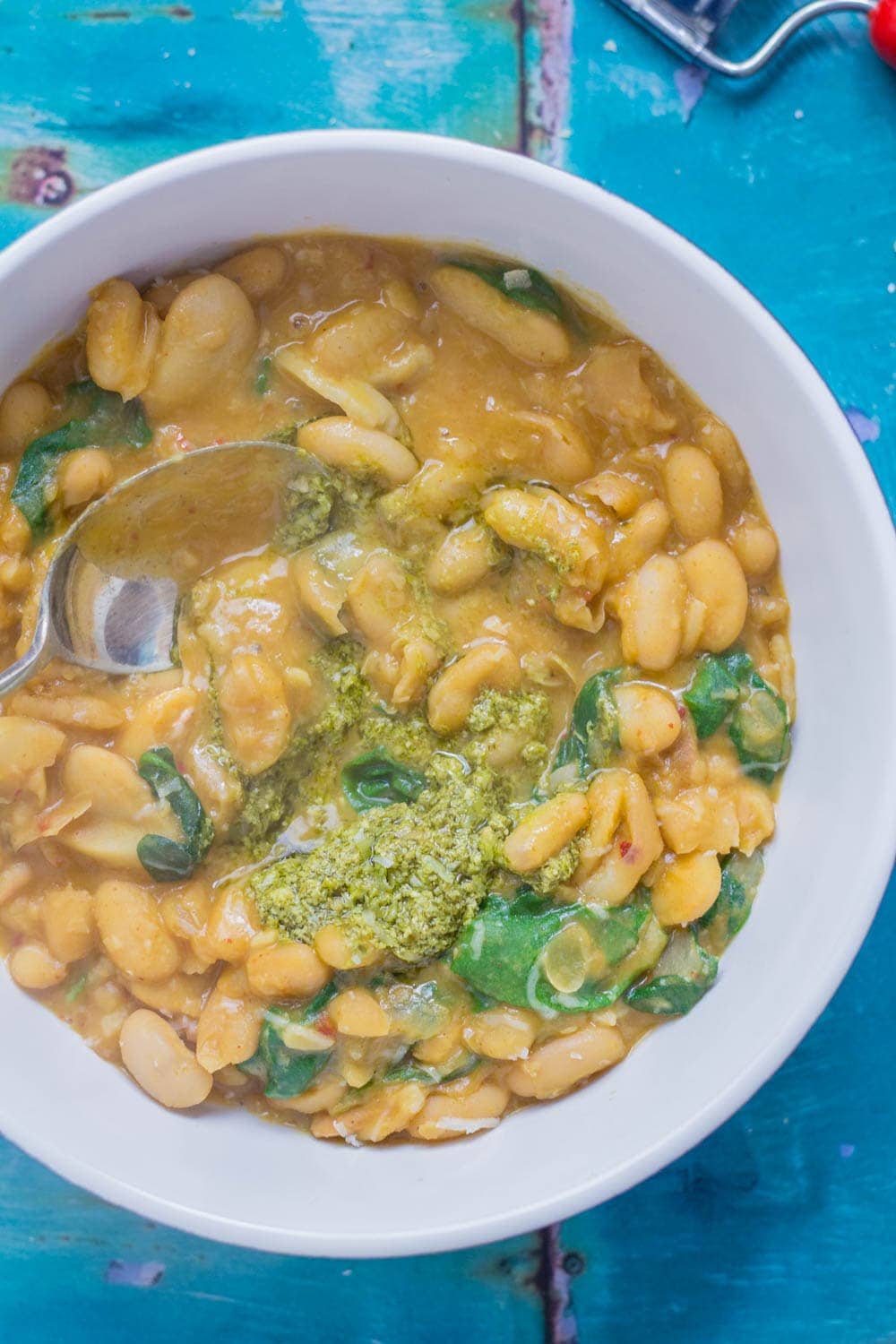 Beans are cooked with bacon, garlic & chicken stock to make this tasty white bean stew. Topped with a homemade pesto for a comforting winter dinner.