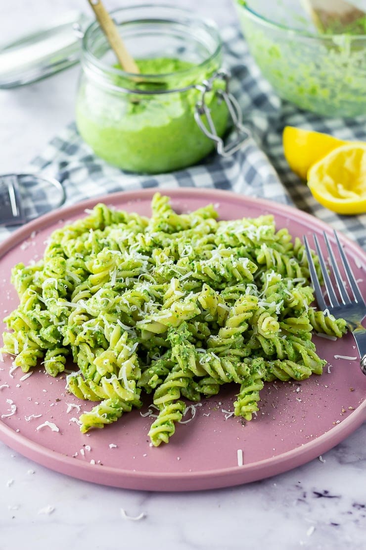 Pink plate of pasta with spinach pesto with lemon and a jar of pesto in the background