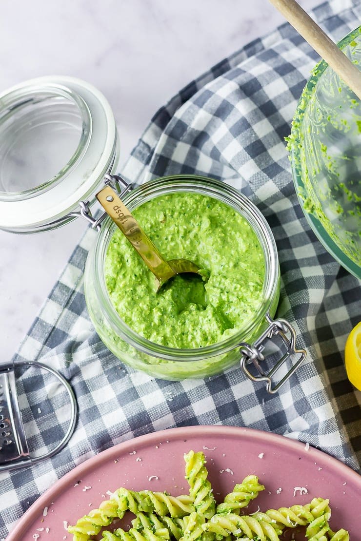 Jar of spinach pesto with feta on a checked cloth over a marble background