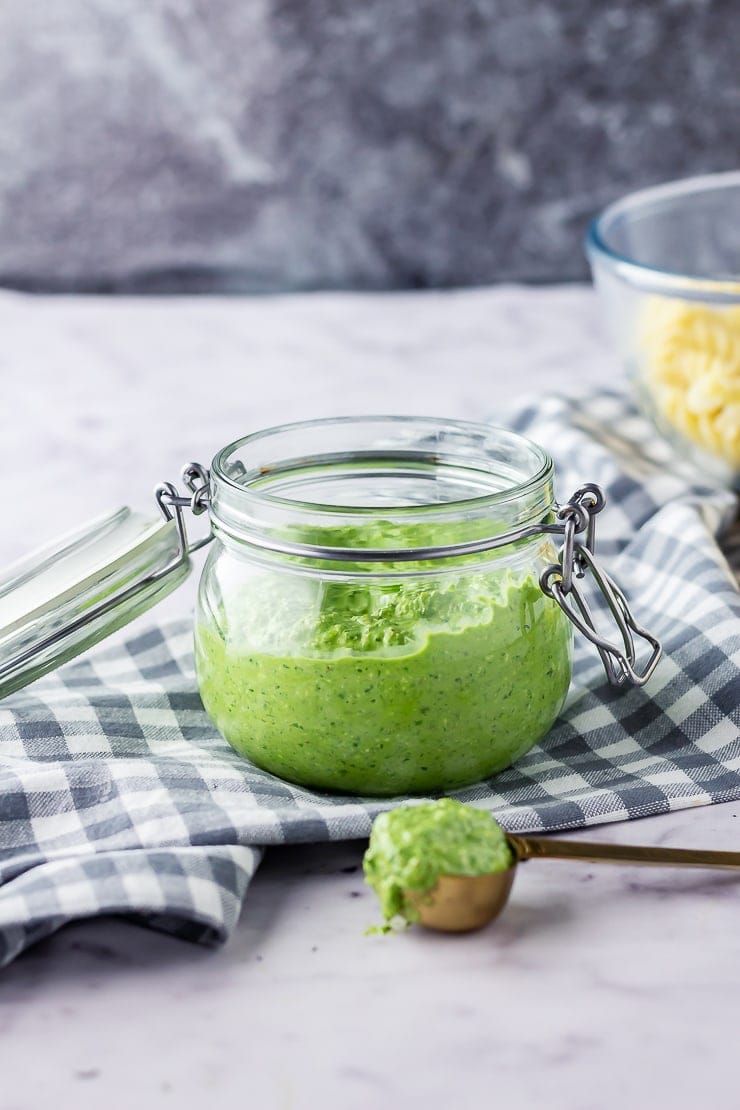 Side shot of a jar of spinach pesto with feta on a checked cloth over a marble background