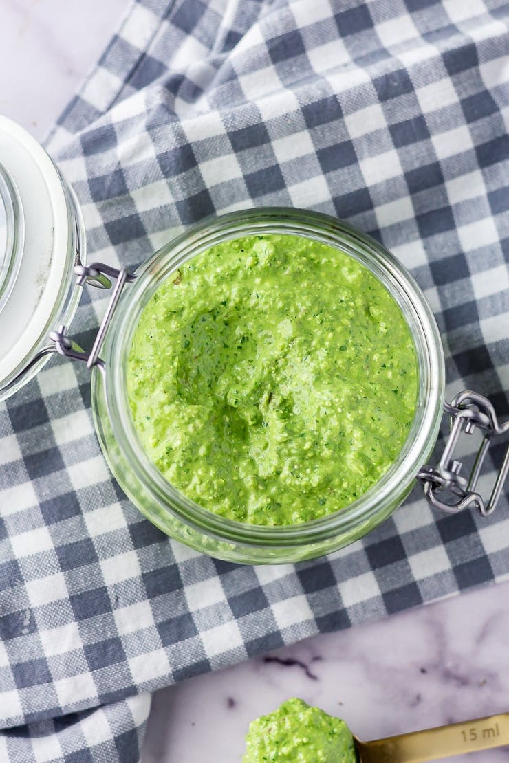 Overhead shot of jar of spinach pesto with feta on a checked cloth