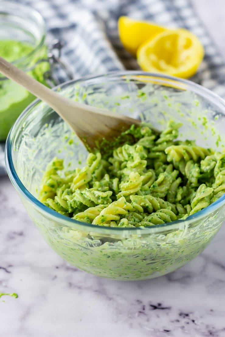 Glass bowl of pasta with spinach pesto with feta on a marble background