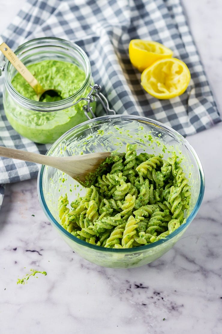Glass bowl of pasta with spinach pesto on a marble background