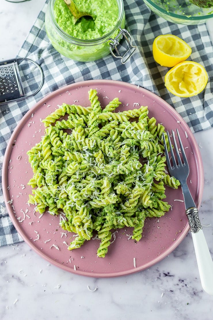 Overhead shot of pasta with spinach pesto on a pink plate over a checked cloth