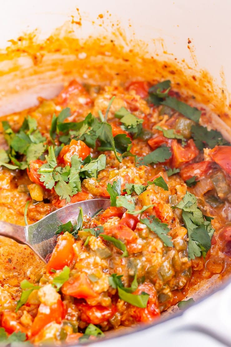 White pot of menemen with a spoon and topped with coriander