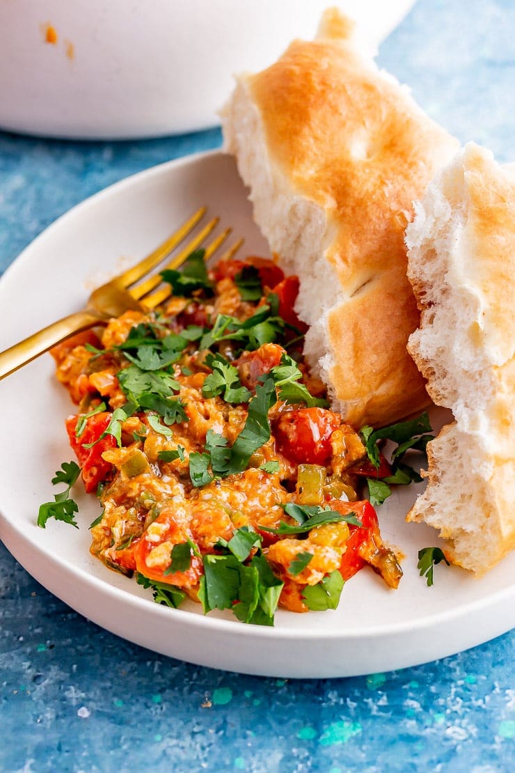 White bowl of menemen with a gold fork and bread on a blue background