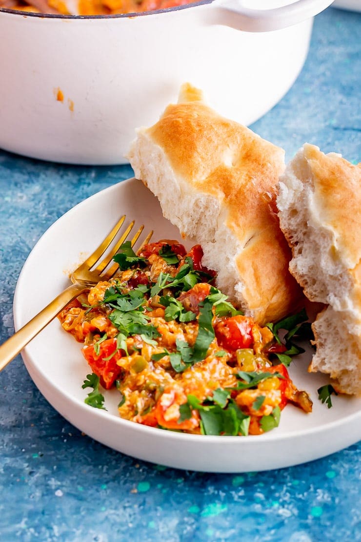 White bowl of menemen with bread and a gold fork on a blue bowl