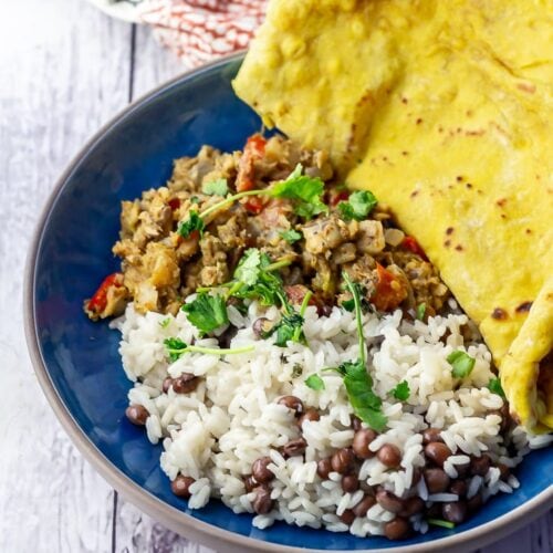Blue bowl of Jamaican fish curry with roti on a white wooden background