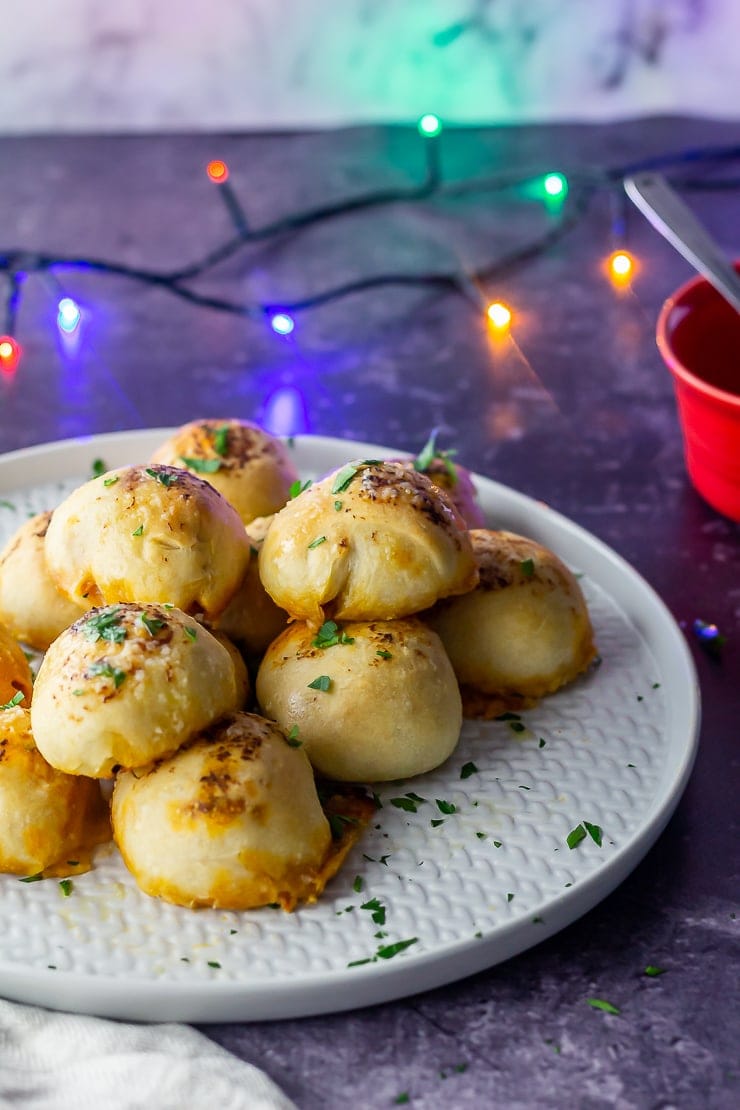 Side on shot of pesto mozzarella stuffed dough balls on a grey plate with a red ramekin in the background