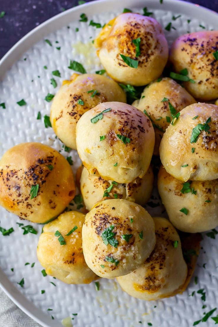 Overhead shot of pesto mozzarella stuffed dough balls on a grey plate with herbs