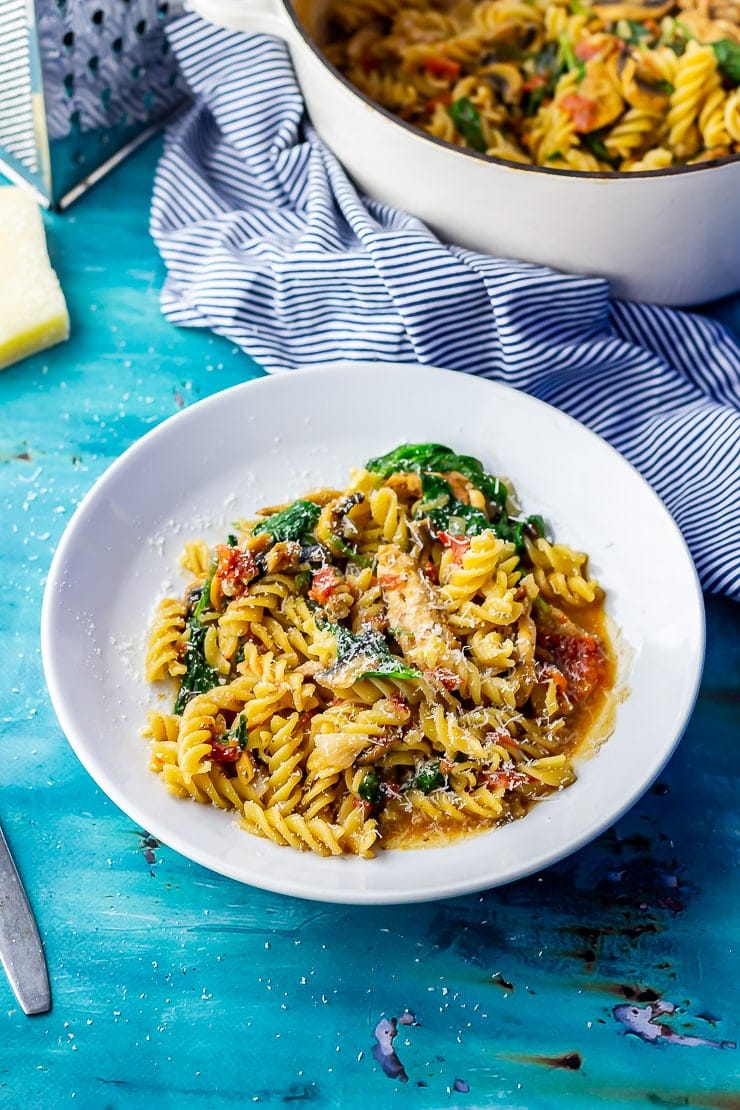 White bowl of one pot pasta on a blue background with a striped cloth