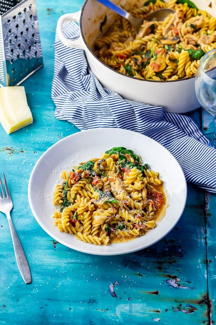 Wide shot of one pot pasta in a white bowl on a blue background with a cooking pot in the background