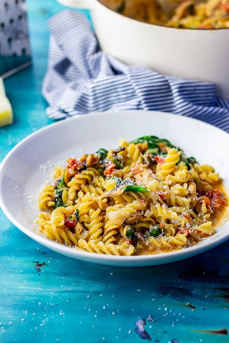 Side shot of a white bowl of one pot pasta on a blue background