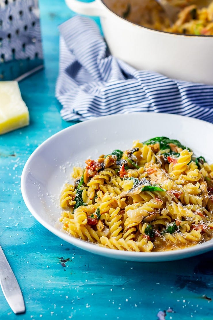 White bowl of one pot pasta on a blue background with a striped cloth