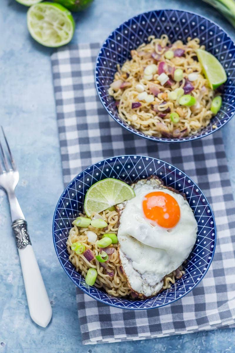 Two blue bowls of peanut noodles with a fork on a blue background