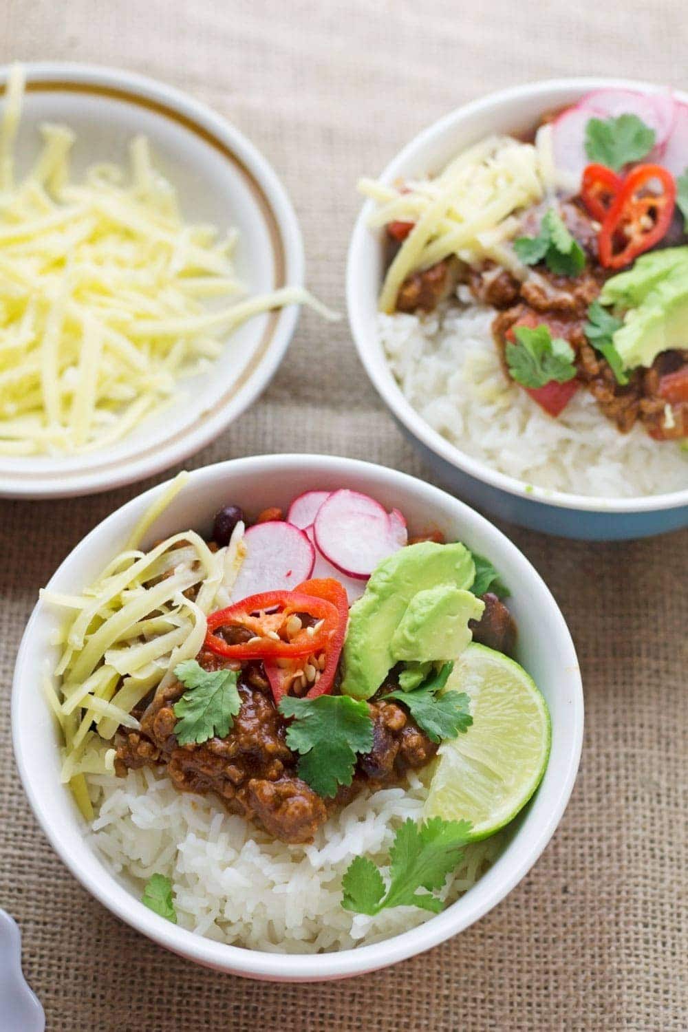 Two bowls of classic beef chilli con carne with grated cheese on a hessian background