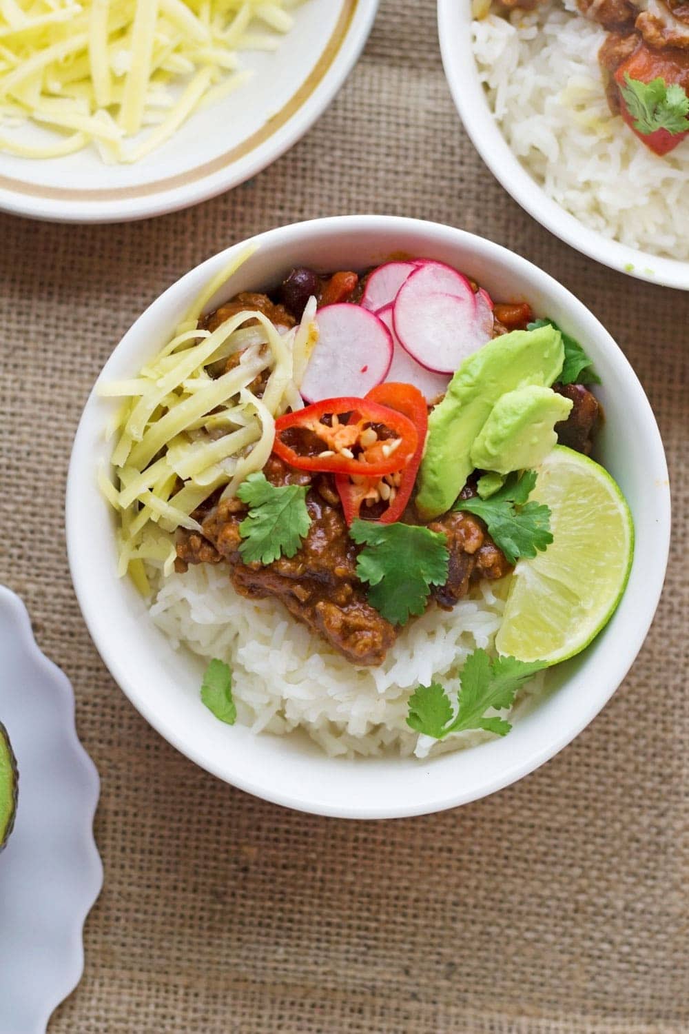 Overhead shot of classic beef chilli con carne with toppings on a hessian background