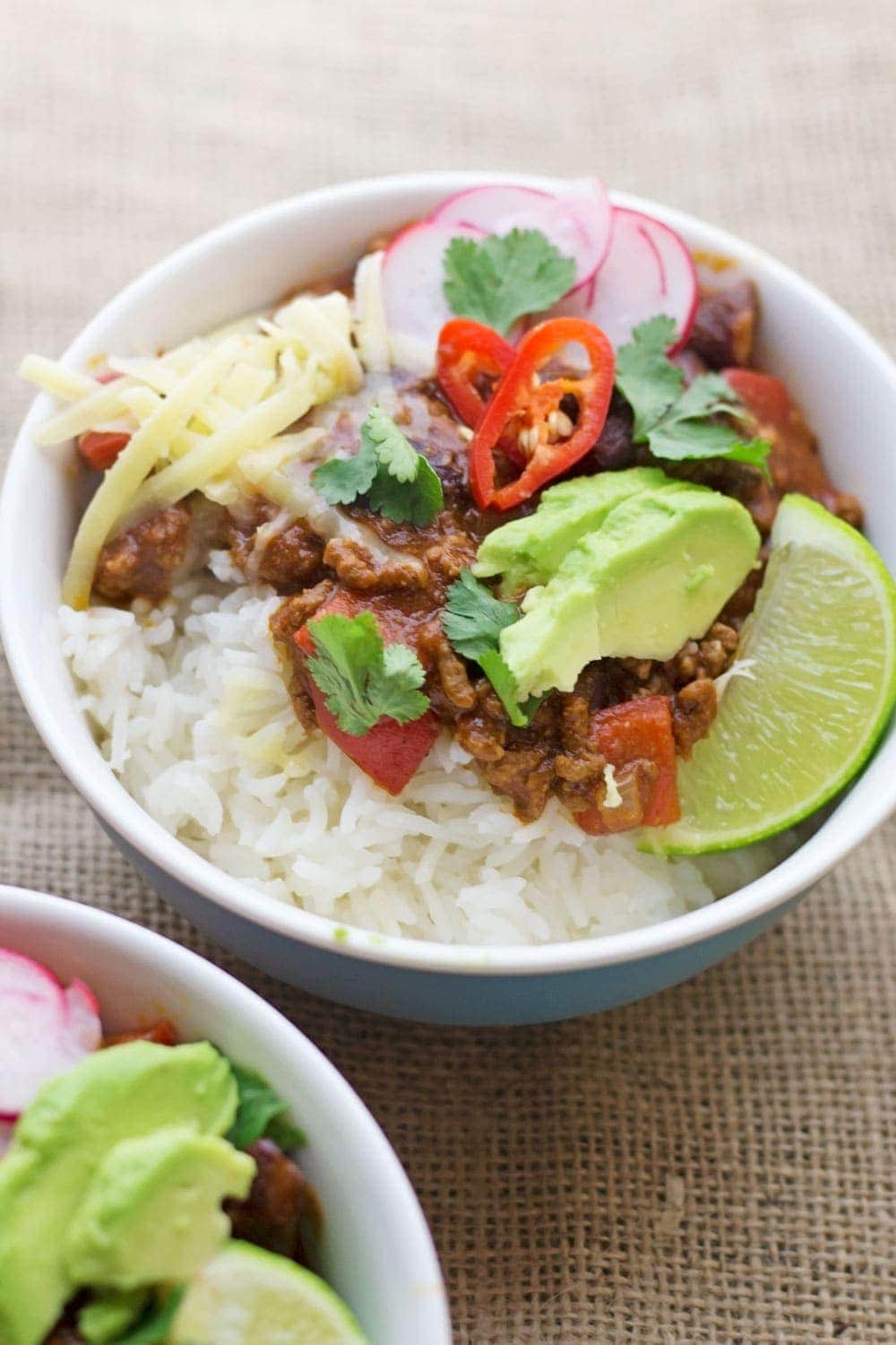 Bowl of classic beef chilli con carne with toppings on a hessian background