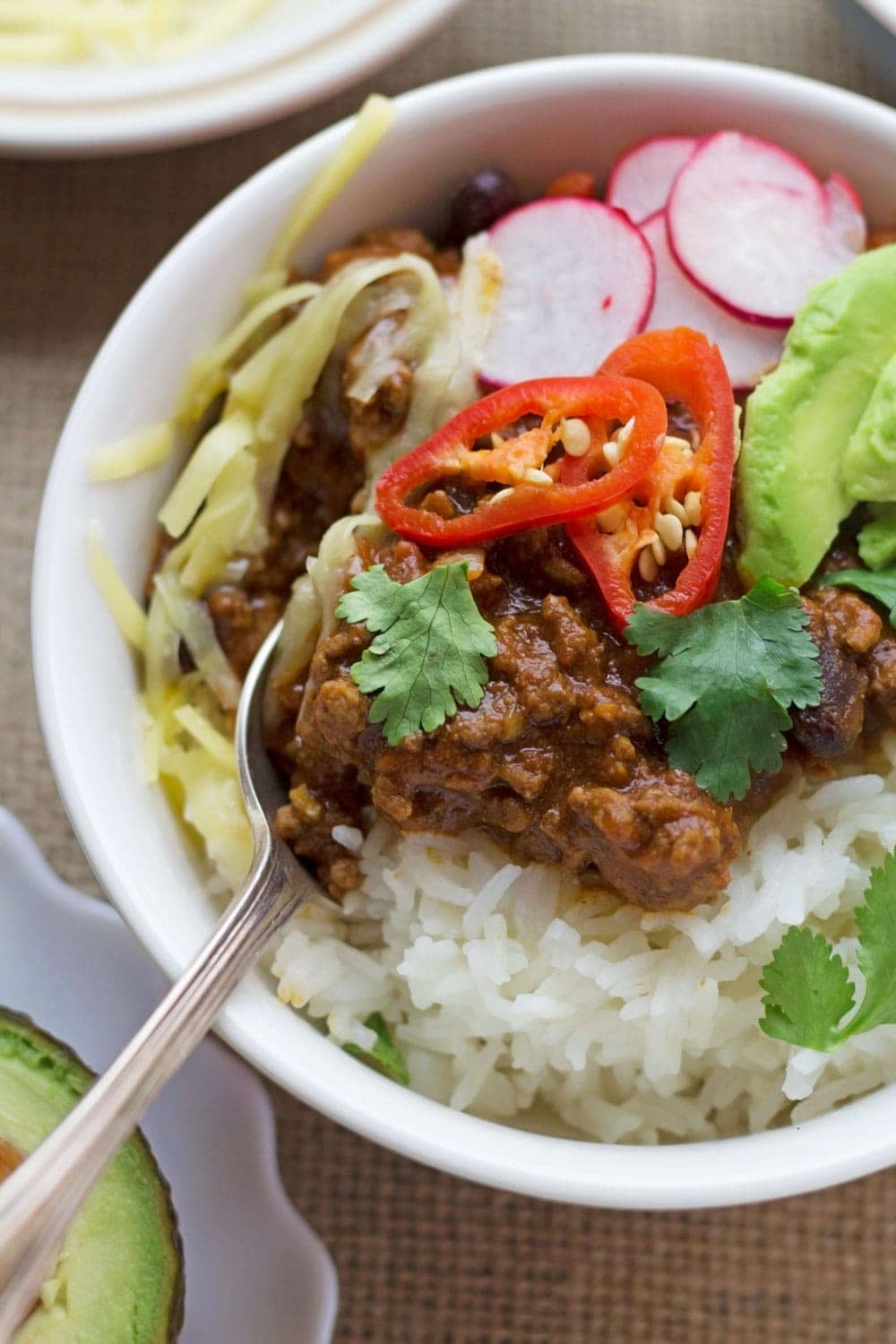 Close up of bowl of classic beef chilli con carne with toppings and a spoon