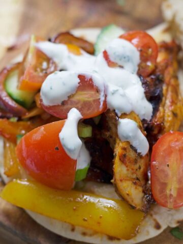 This sheet pan Greek chicken is served in a flatbread with garlicky marinated tomatoes and an incredible herby sour cream sauce!
