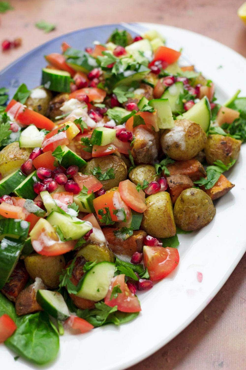 Roast potato salad with cucumber, tomatoes and pomegranate on a white dish