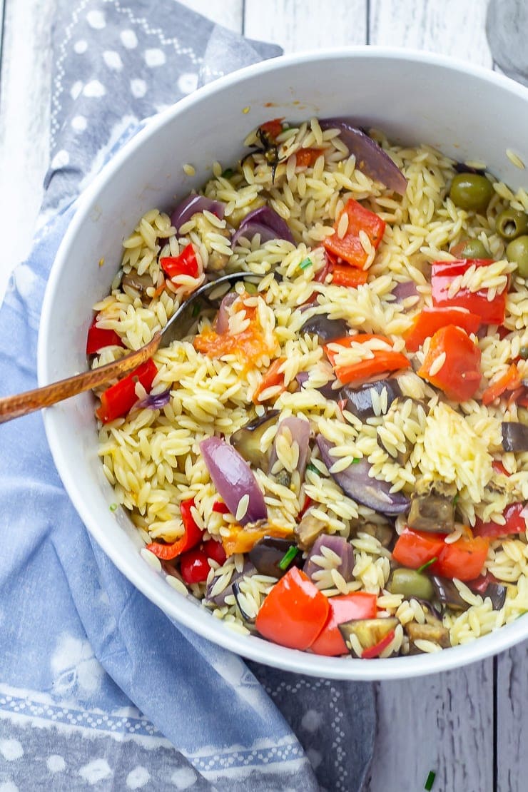 Overhead shot of summer orzo salad with a blue cloth and white wooden background