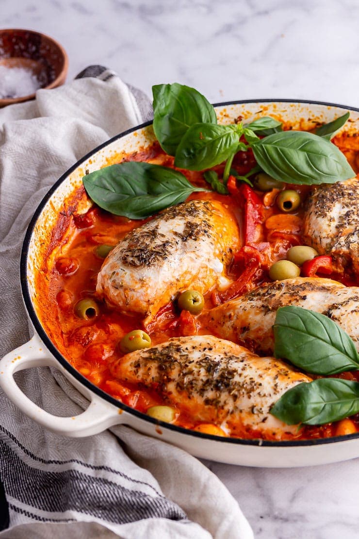 Creamy chicken in a white skillet with basil on a marble background