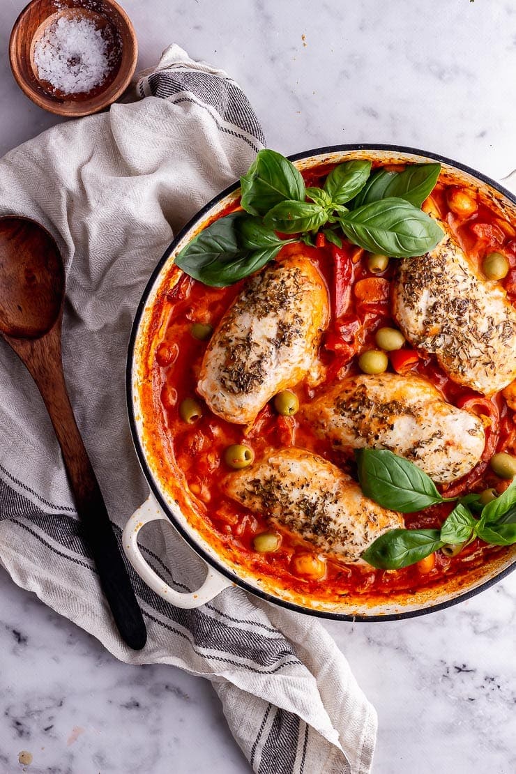 Overhead shot of Italian sauce with chicken on a beige cloth with a wooden spoon