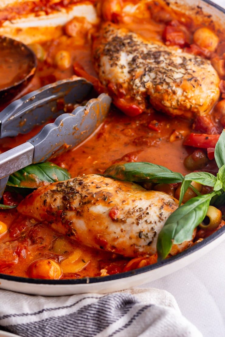 Close up of creamy Italian chicken with tongs and a cream cloth