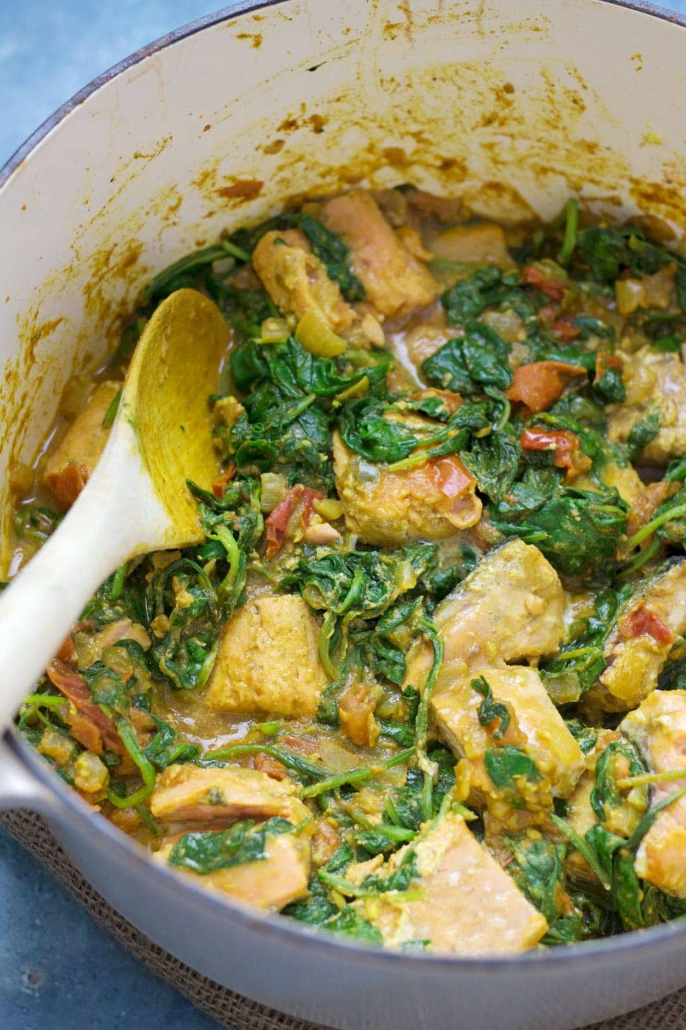 Close up of salmon curry in a pot with a wooden spoon