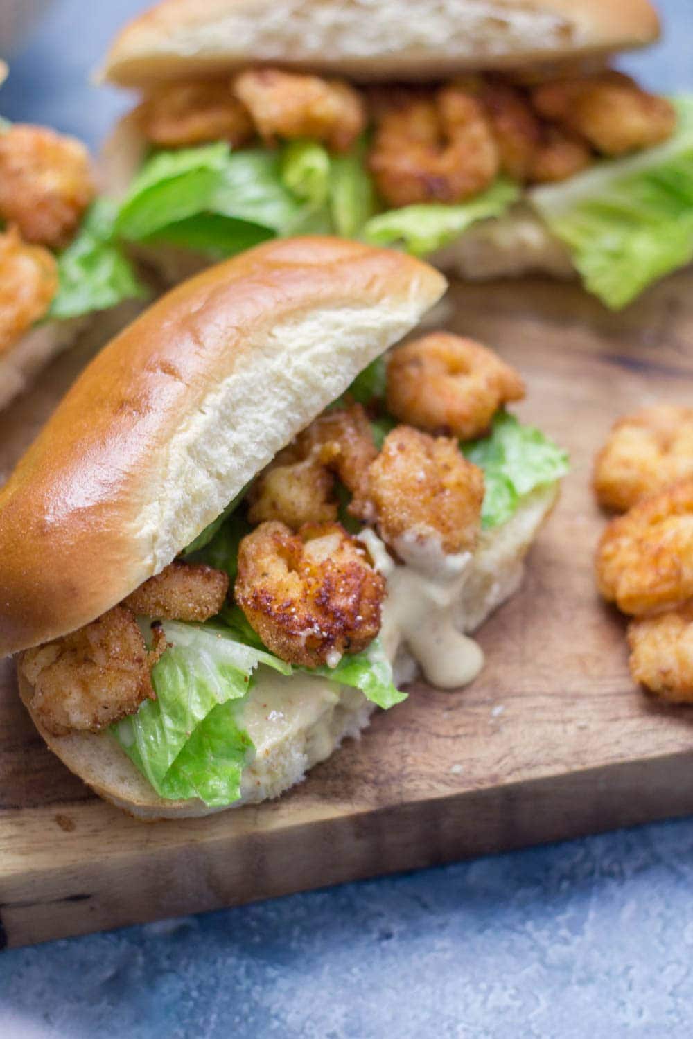 Prawn po' boys are made up of crispy prawns nestled into a bread roll with crunchy lettuce & tangy Cajun sauce. Bring a taste of New Orleans to your home! #sandwich #seafood #poboy #cajunfood #recipe