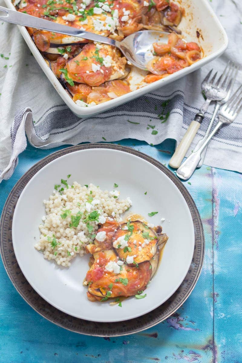 Overhead shot of aubergine bake in a bowl with forks on a blue surface