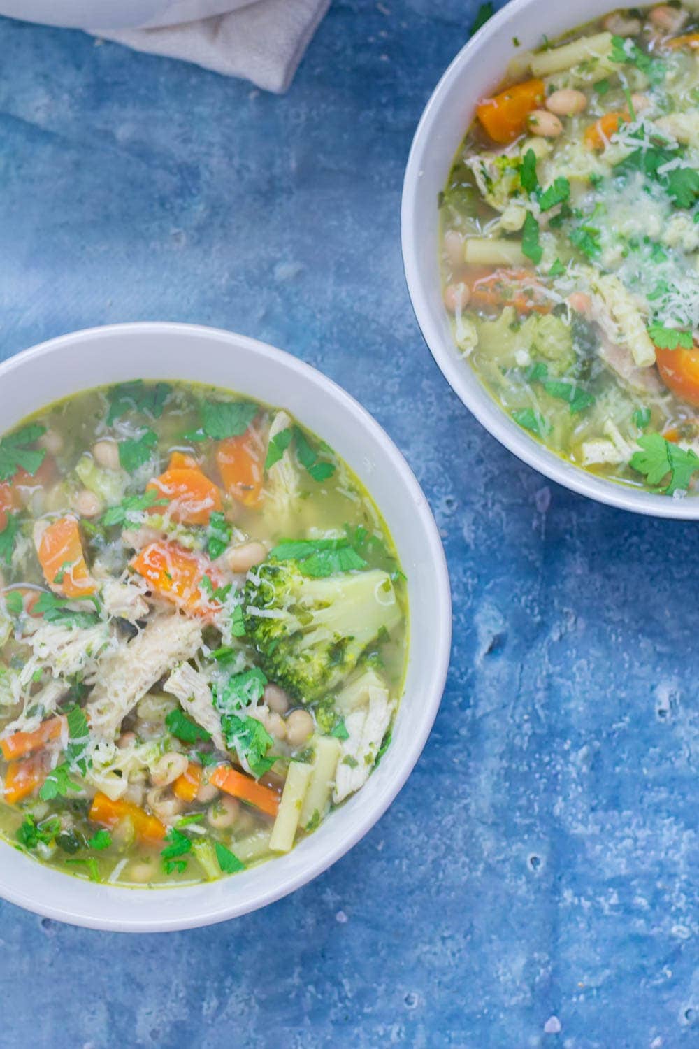 Two bowls of chicken and vegetable soup on a blue surface