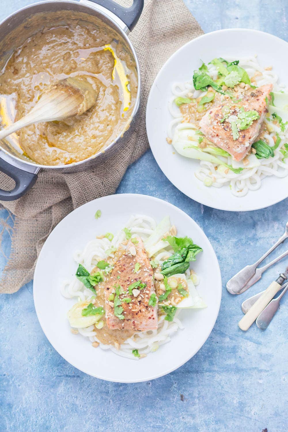 Overhead shot of two bowls of peanut salmon noodles on a blue background with peanut sauce