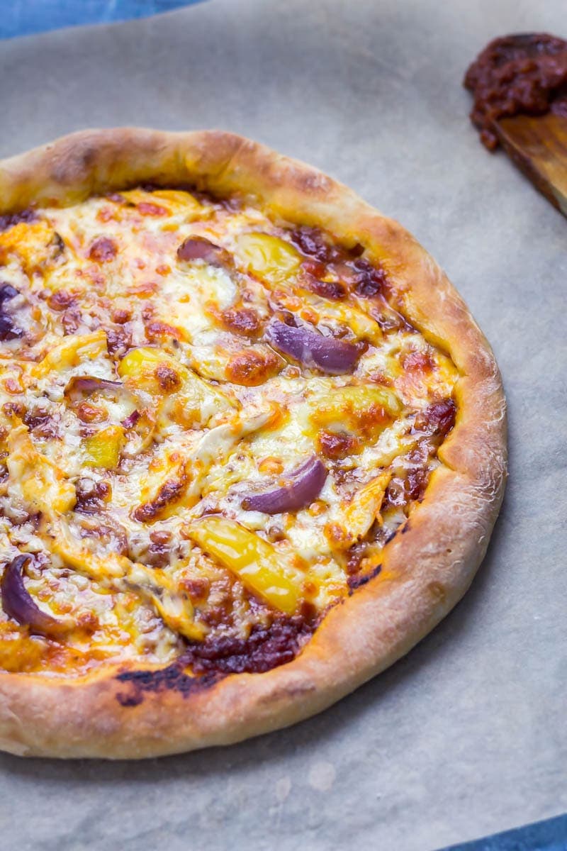 Angled shot of stuffed crust pizza with chipotle chicken and a wooden spoon with chipotle sauce