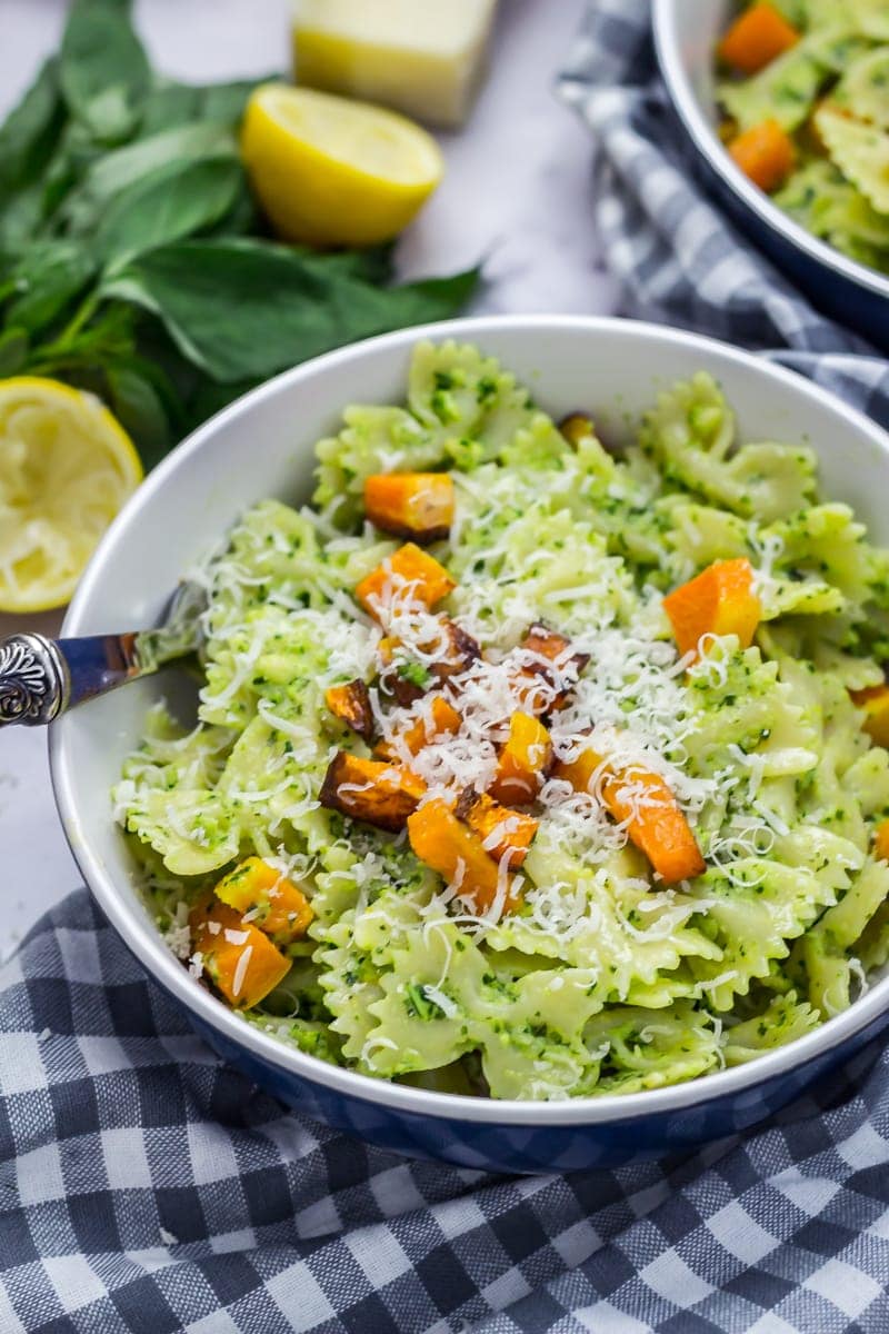 Kale pesto pasta in a bowl topped with butternut squash and parmesan on a checked cloth