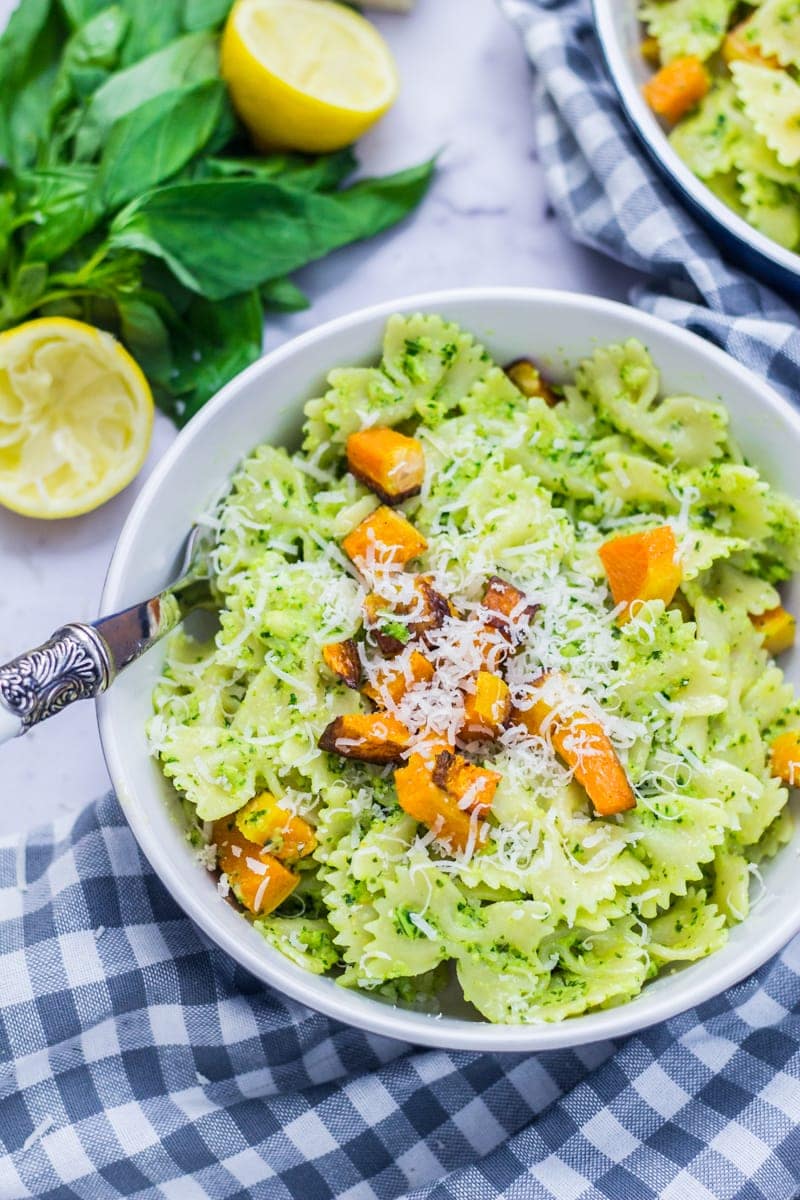 Kale pesto pasta with butternut squash on a checked cloth with basil and lemon