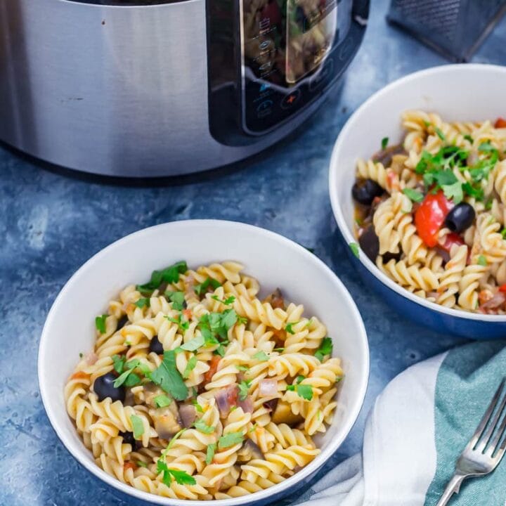 Two bowls of pasta with olives, pepper and aubergine sprinkled with parsley and pressure cooker in the background
