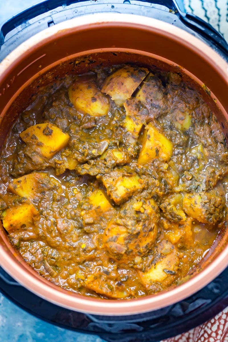 Close up of saag aloo in a pressure cooker with a blue background