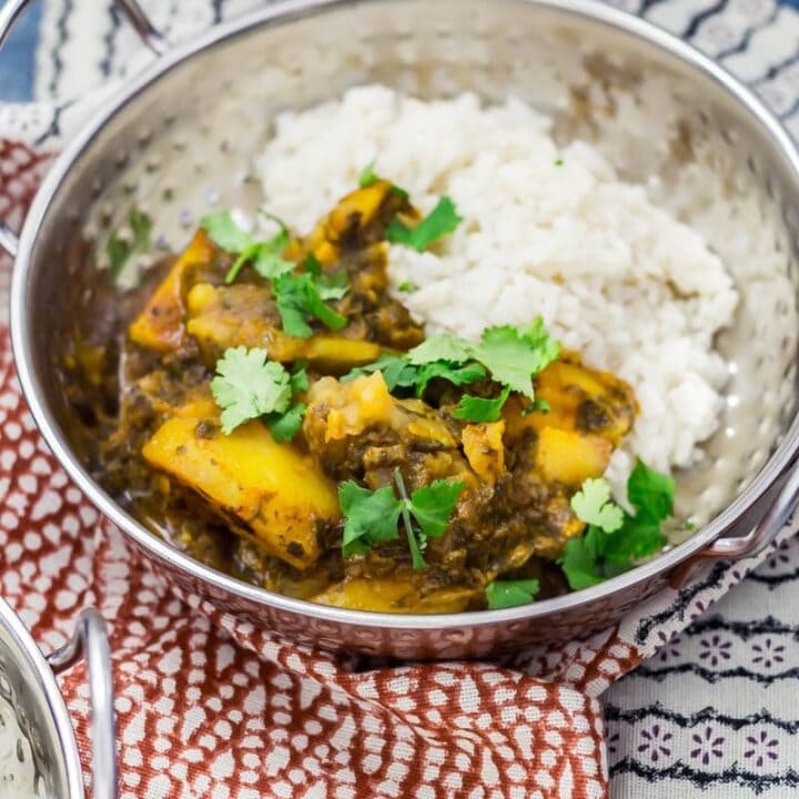 Metal bowl of saag aloo with rice, topped with coriander leaves on a patterned tea towel