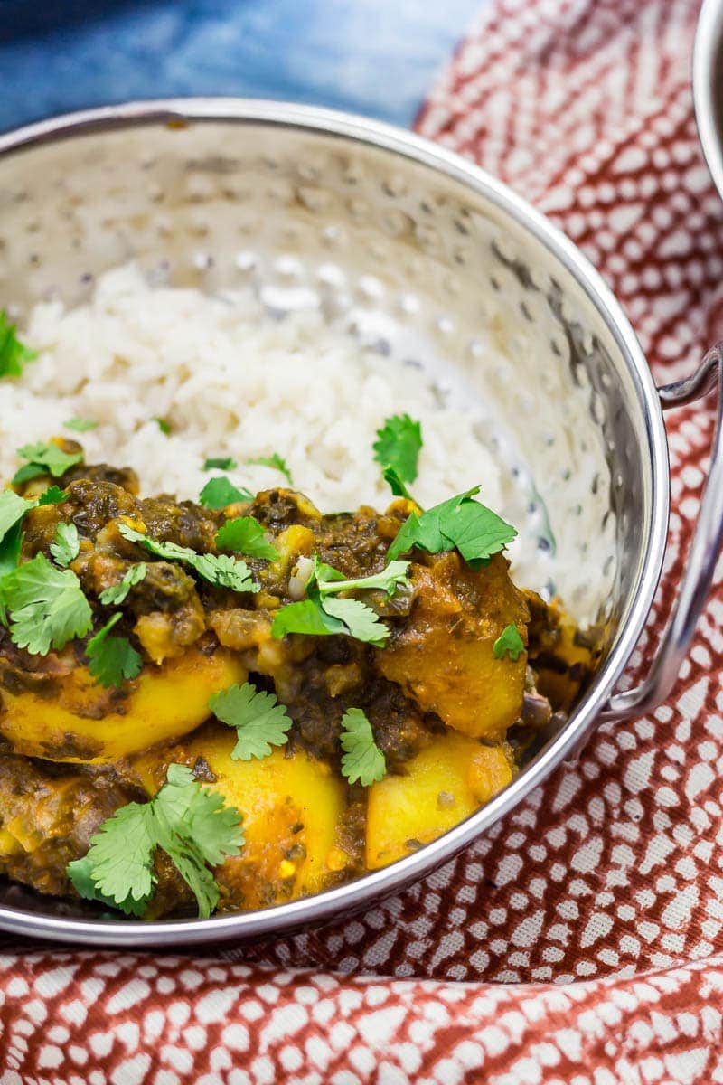 Metal bowl of saag aloo with white rice on a patterned towel