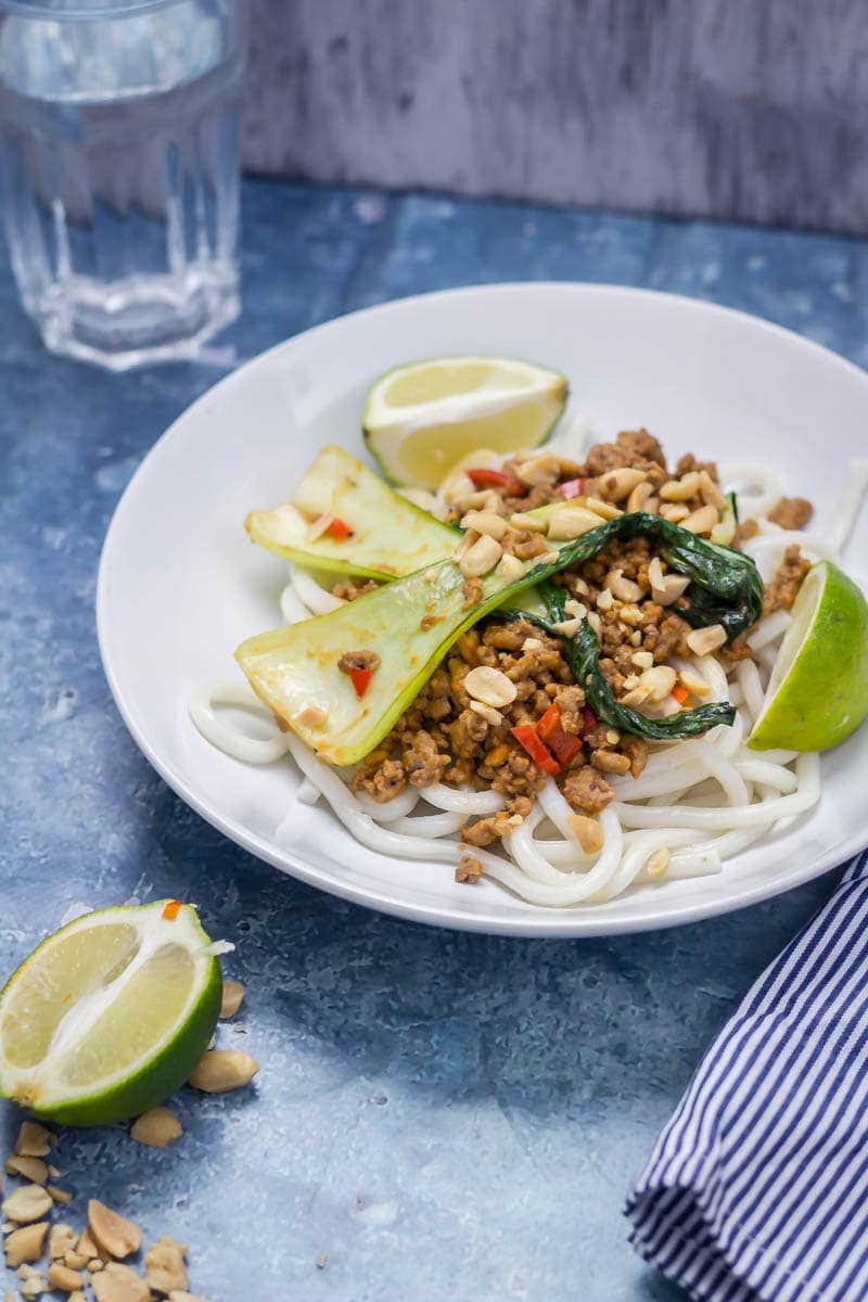 Udon noodle stir fry with turkey mince in a white bowl with a lime half and peanuts in the foreground