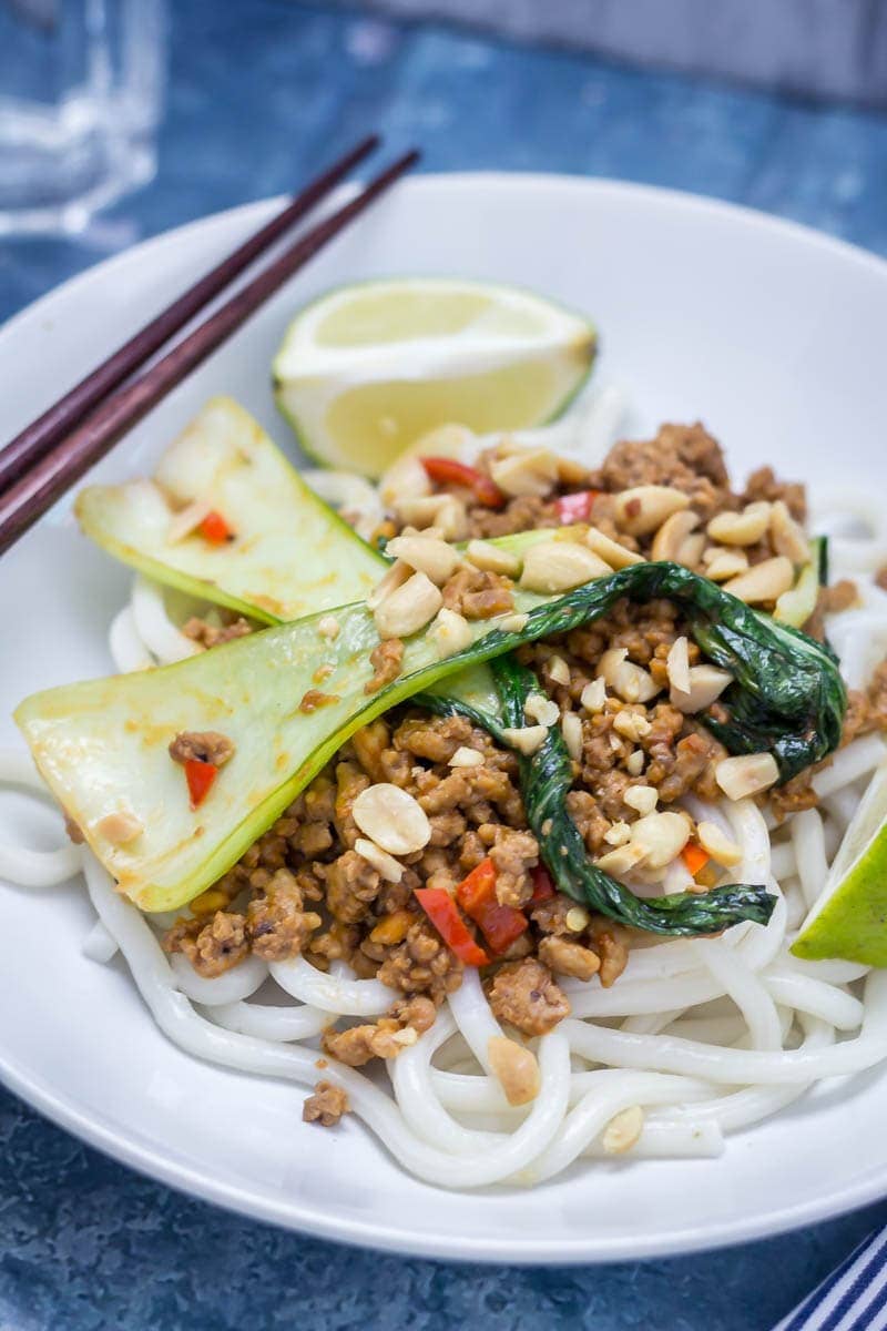 Udon noodle stir fry in a white bowl with turkey mince, pak choi and lime wedges with chopsticks in the background