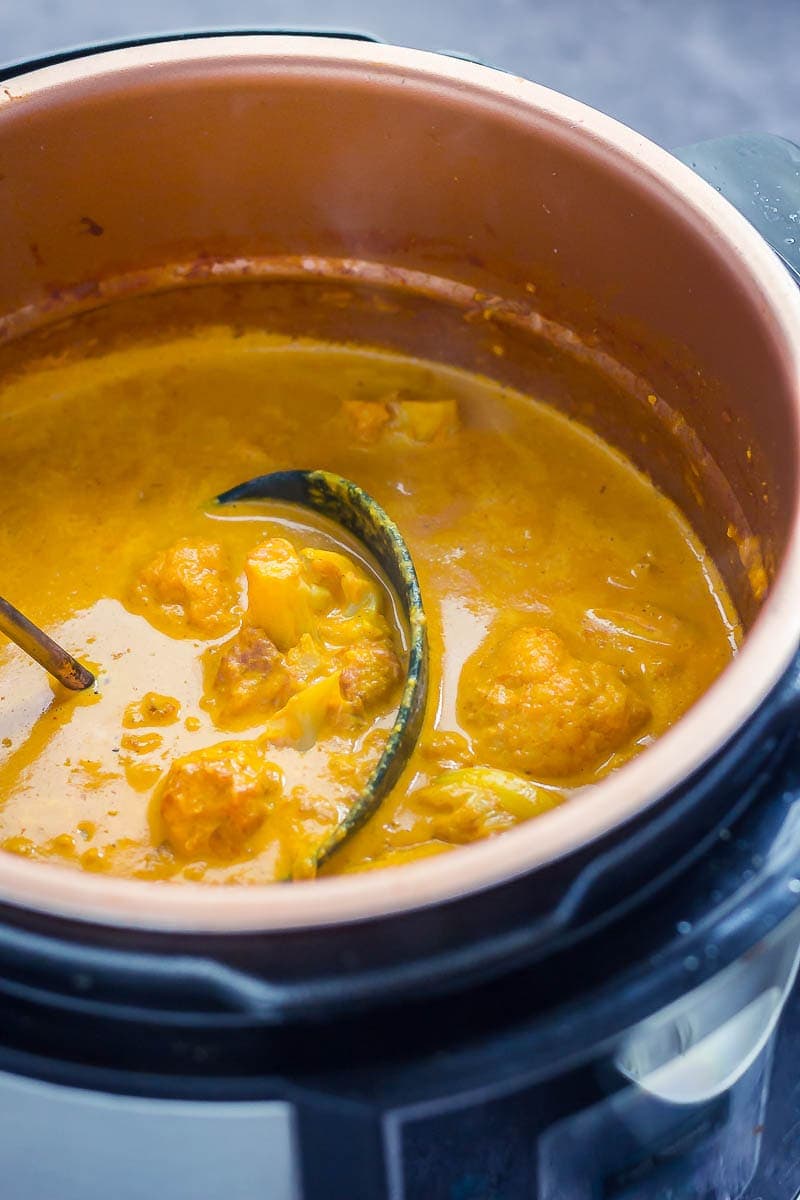 Creamy cauliflower curry in a pressure cooker with ladle