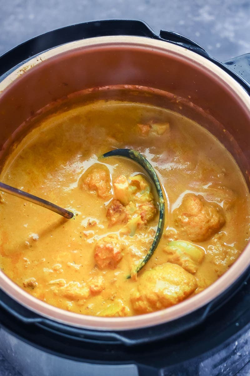 Creamy cauliflower curry in the pressure cooker with a ladle