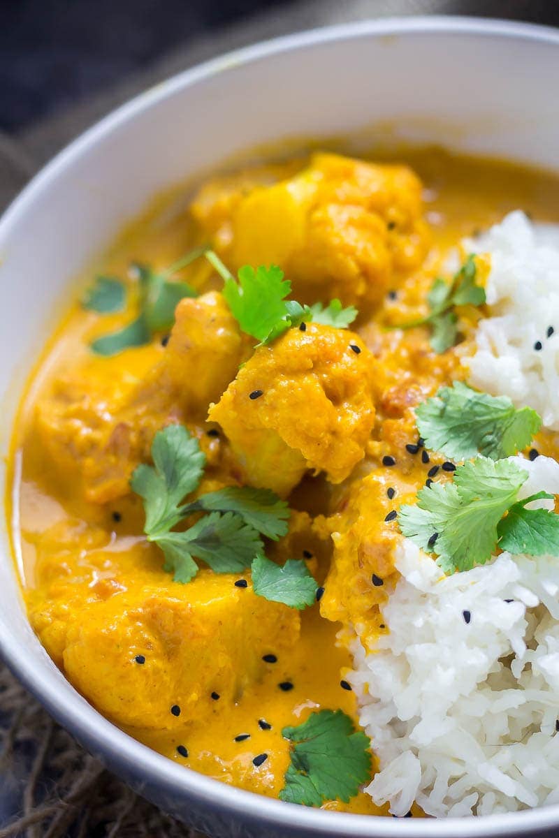 Close up of a bowl of creamy cauliflower curry with rice and topped with nigella seeds and coriander leaves