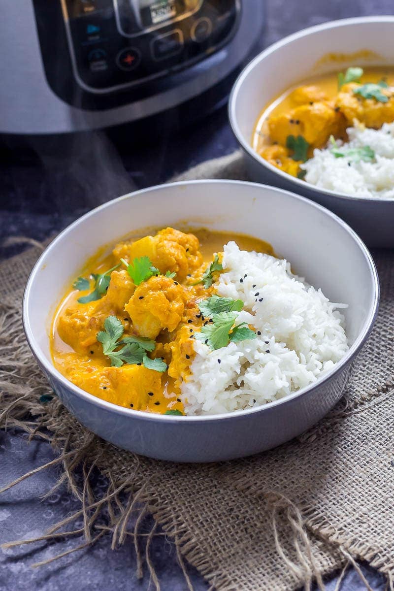 Two bowls of creamy cauliflower curry with the pressure cooker in the background