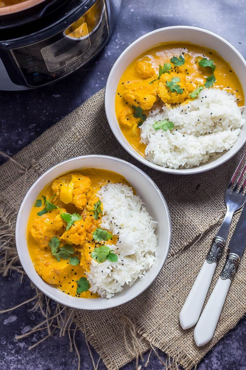 Creamy cauliflower curry in two bowls on hesian with a knife and fork and dark background