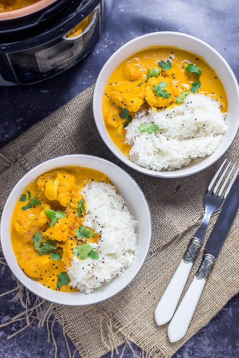 Overhead photo of two bowls of creamy cauliflower curry on a dark background with a knife and fork