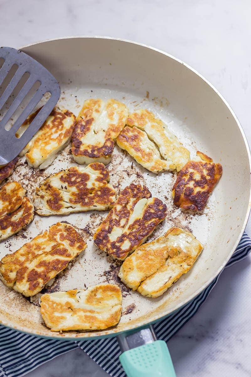How to cook halloumi. Fried halloumi in a ceramic frying pan on a marble background